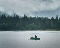 Pêcheur en barque sur un lac brumeux bordé de conifères