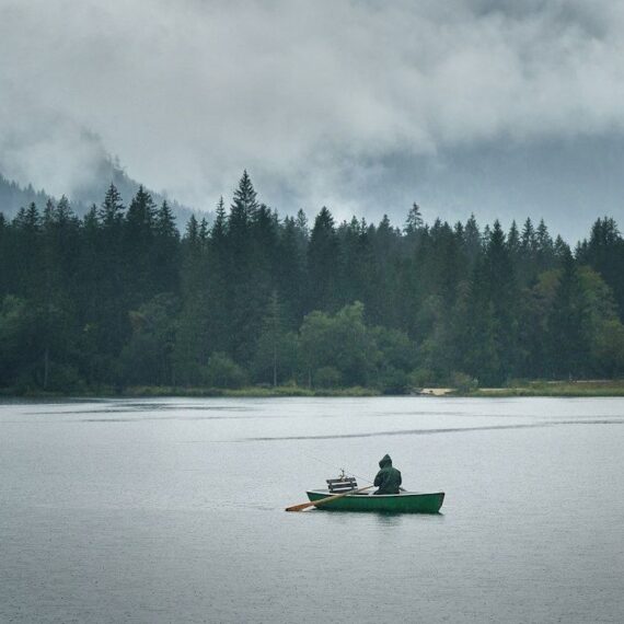 Pêcheur en barque sur un lac brumeux bordé de conifères